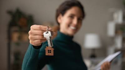 Eine Frau hält lächelnd einen Schlüssel in die Kamera, Symbolfoto für Immobilienerwerb 