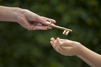 Hände einer älteren Person geben einen goldenen Schlüssel in die Hände einer jüngeren Person. Es sind nur die Hände und der Schlüssel zu sehen.