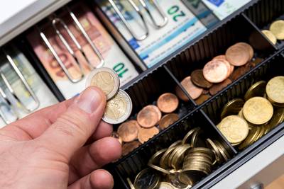 Registrierkasse mit Münzen und Papiergeld, eine Hand hält zwei Zwei-Euro-Münzen